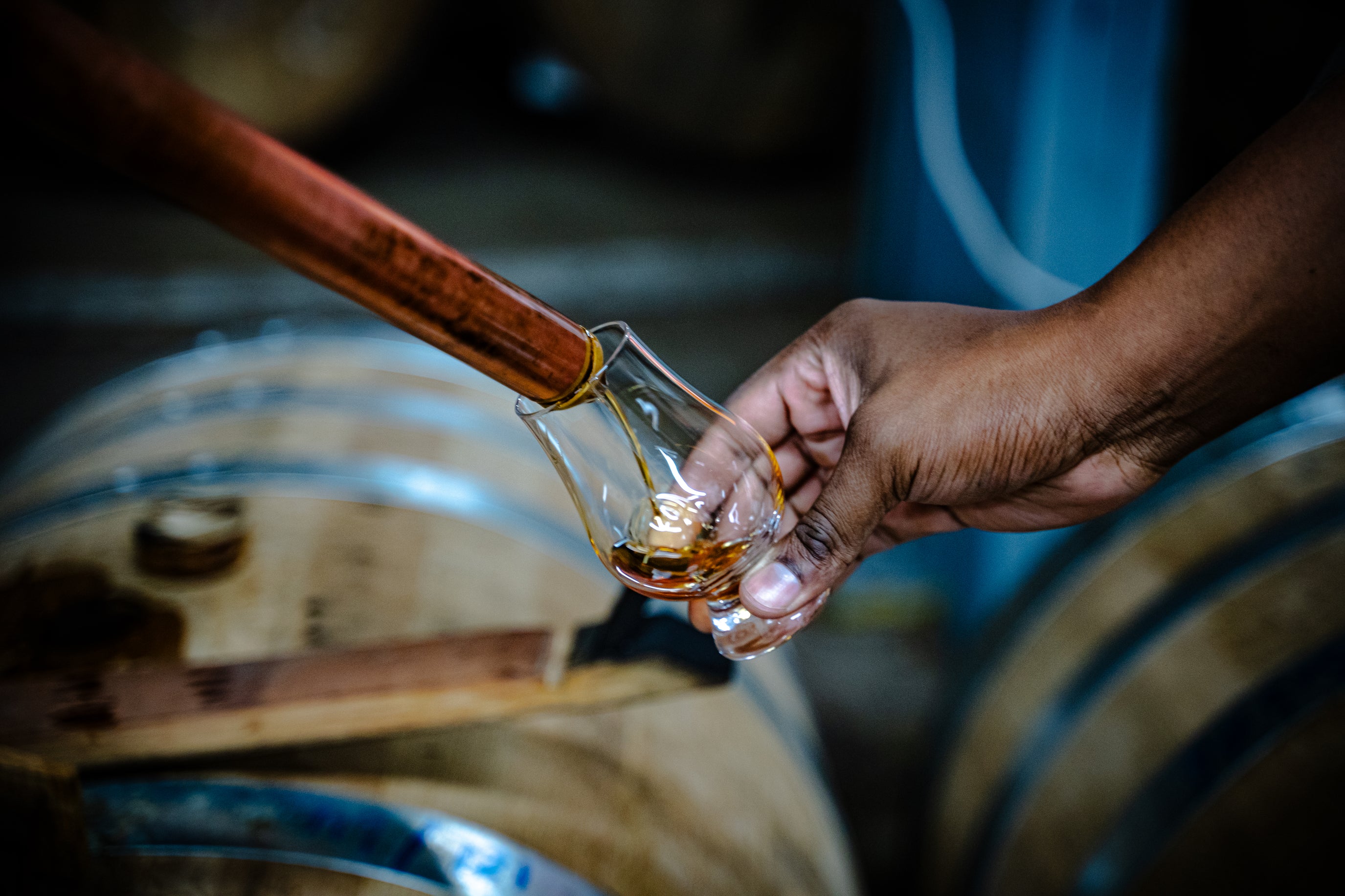 A whiskey thief pouring a sample of River City Whiskey from the barrel into a glencairn