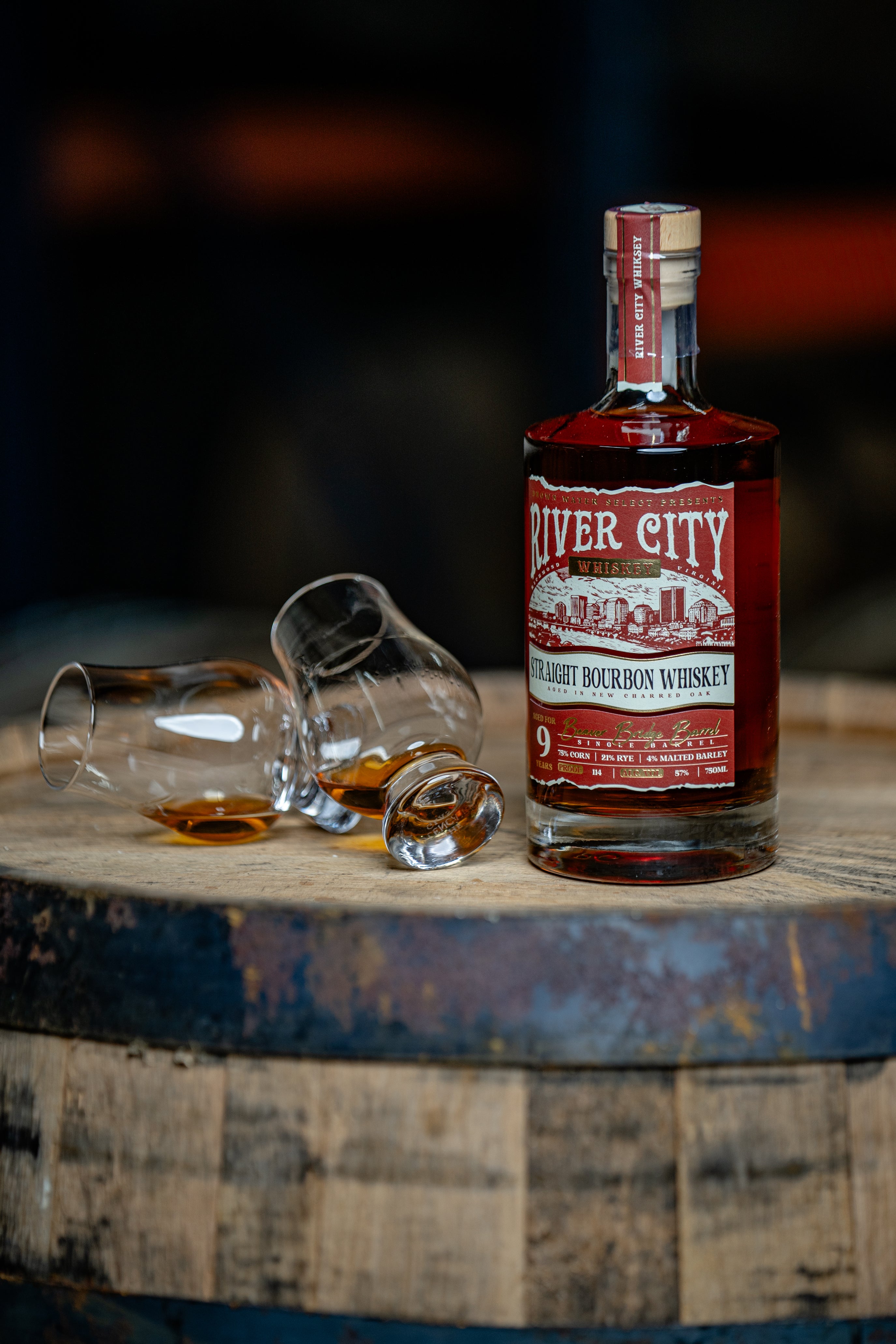 Two tipped over glencairns of next to a bottle of River City Whiskey, sitting on top of a barrel