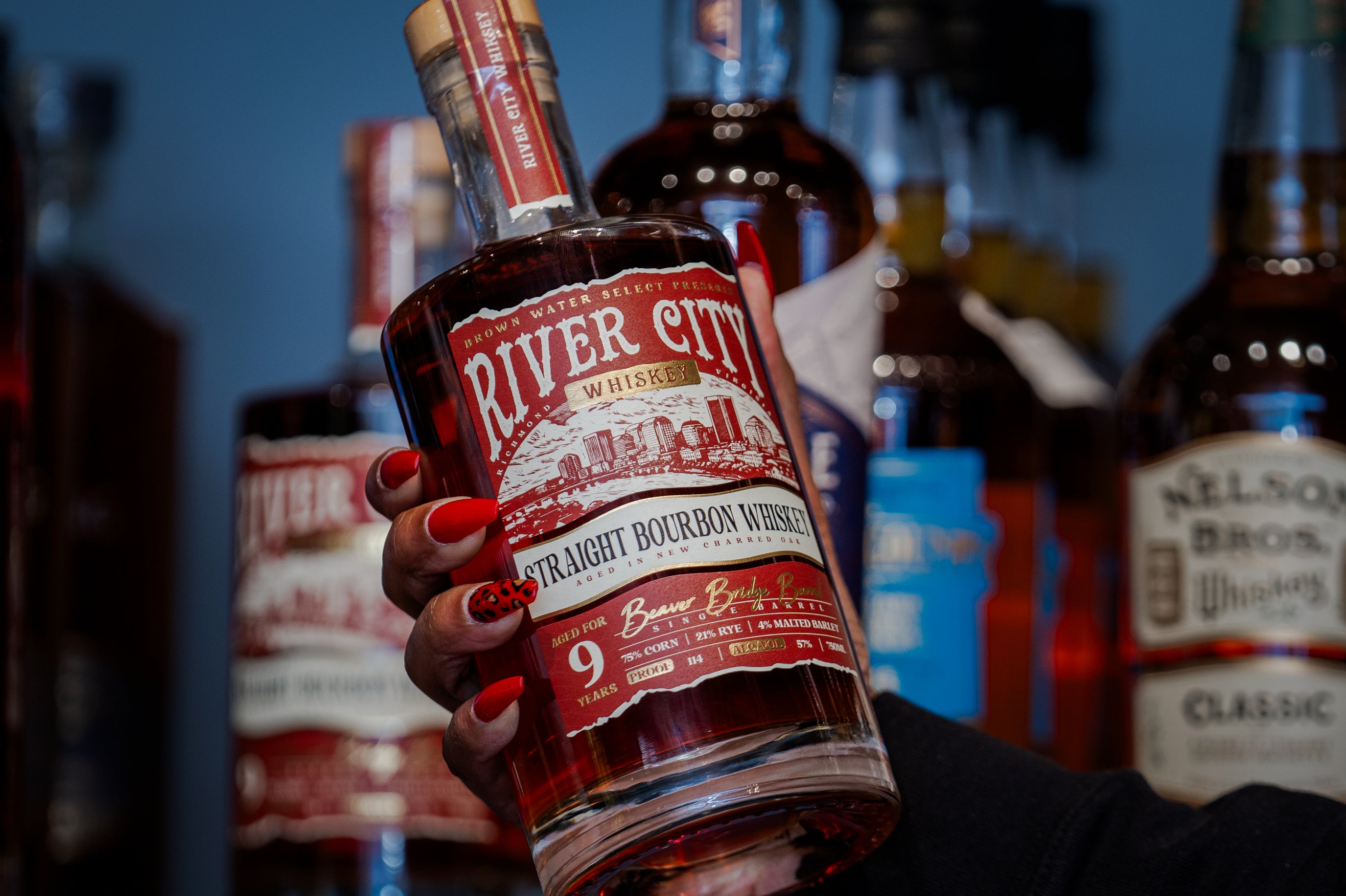 A well-maincured woman's hand pulling a bottle of River City Whiskey off the shelf